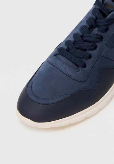 Baskets bleu marine avec une tige en cuir lisse, lacets texturés et semelle en caoutchouc crème. Présente des détails de couture et un design de bout arrondi.