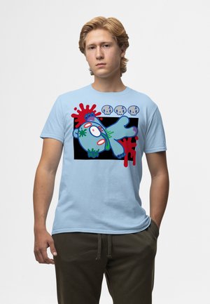 Giovane uomo che indossa una camicia azzurro chiaro con la grafica di un orso zombie in stile cartone animato e macchie rosse su sfondo nero.