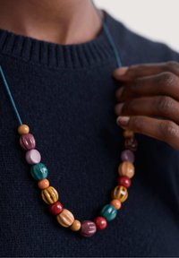 Helmed kaelakee, millel on värvikad ümarad ja ovaalsed puidust helmed roosa, teal, punase, kollase ja pruunina, stringitud sinise nööriga.