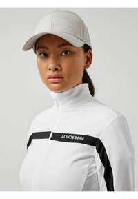 Giacca bianca con zip e dettagli neri, logo; tessuto leggero; abbinata a un cappellino grigio chiaro con un design a motivo sottile.