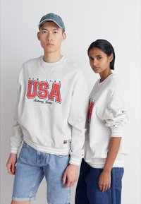 Felpe grigio chiaro con la scritta "NEW YORK USA" in lettere rosse. Presentano polsini e orlo a coste, abbinate a pantaloni corti di denim. Vestibilità rilassata.