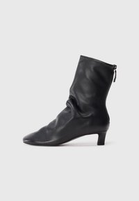 Botte en cuir noire mi-mollet avec un design plissé, orteil pointu et un petit talon carré. Présente une fermeture zippée à l'arrière.