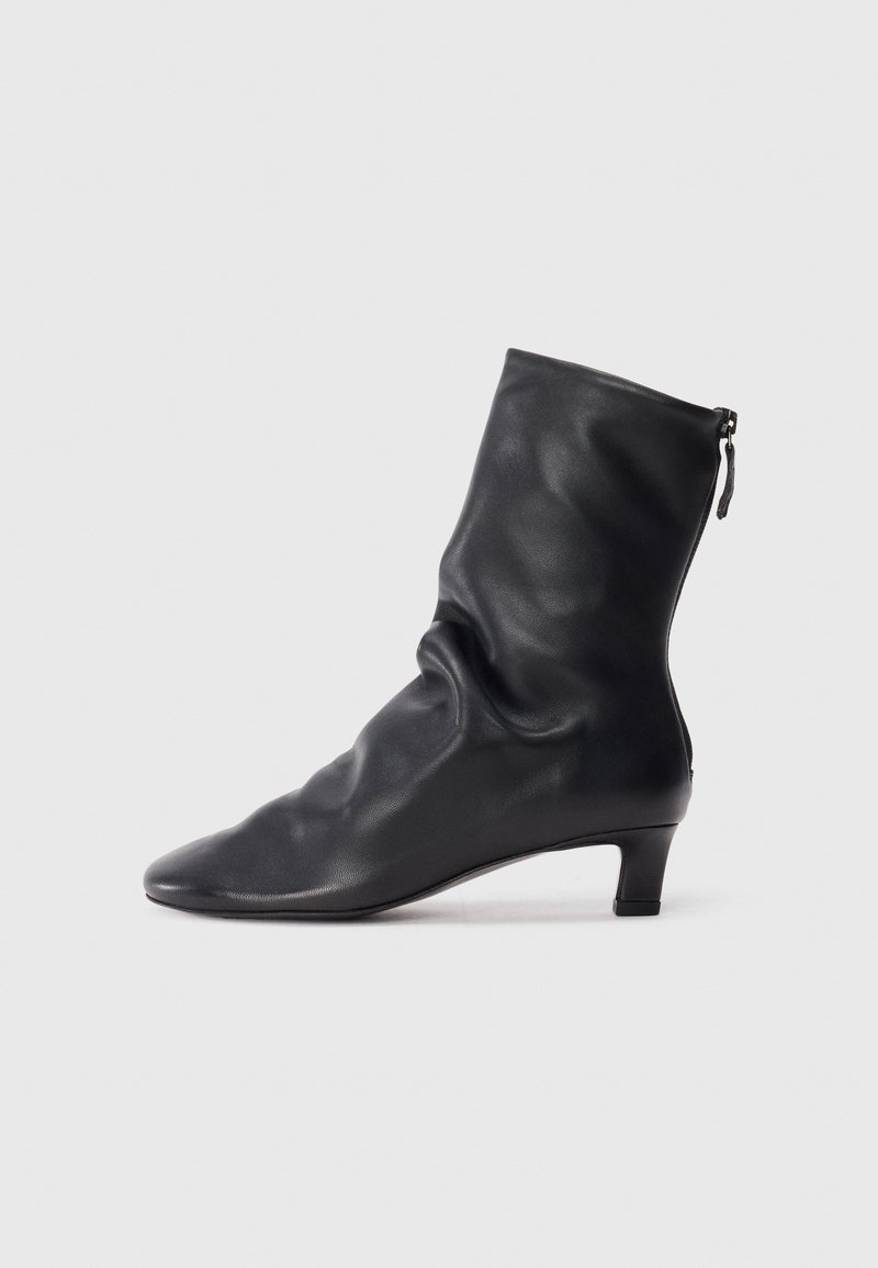 Botte en cuir noire mi-mollet avec un design plissé, orteil pointu et un petit talon carré. Présente une fermeture zippée à l'arrière.