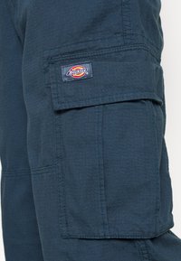 Marinblå twill cargobyxor med en synlig Dickies-logotyp. Har flera fickor och en strukturerad yta. Förstärkt sömdetalj.