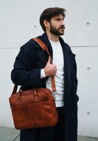 Brown leather briefcase featuring a zip closure, dual top handles, and an adjustable shoulder strap. Smooth texture with subtle stitching details.