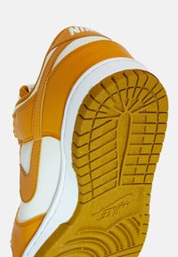 Teniska Nike v oranžové a bílé kůži. Má texturovanou podrážku s výrazným vzorkem a prošitý design podél boků.