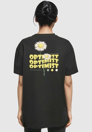 Sort bomulds T-shirt med et grafisk design af hvide margueritter og teksten "OPTIMIST" i gul. Løs pasform, rund hals, korte ærmer.