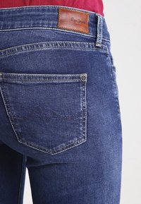 Mörkblå denimjeans med en läderlogotags på midjan och en bakficka med kontrasterande sömmar.