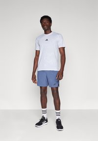 Gray athletic t-shirt with black logo, paired with blue shorts featuring logo, black athletic shoes, and striped black-and-white socks.