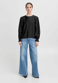 Blusa nera a maniche lunghe con scollo rotondo e spalle a sbuffo, abbinata a jeans a gamba larga di un blu chiaro e décolleté neri appuntiti.