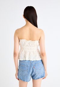 Top peplum in pizzo off-white, con scollatura a volant e finitura testurizzata, abbinato a shorts in denim azzurro chiaro.