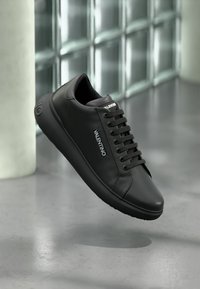 Schwarze Ledersneaker mit glatter Oberfläche, runder Zehenpartie und flachem Schnürsenkelsystem, versehen mit einem Logo-Akzent an der Seite und schwarzen Schnürsenkeln.