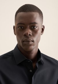 Camicia nera con colletto, dalla texture sottile, dettagli con bottoni e vestibilità slim, indossata da un modello con capelli corti e scuri su uno sfondo neutro.