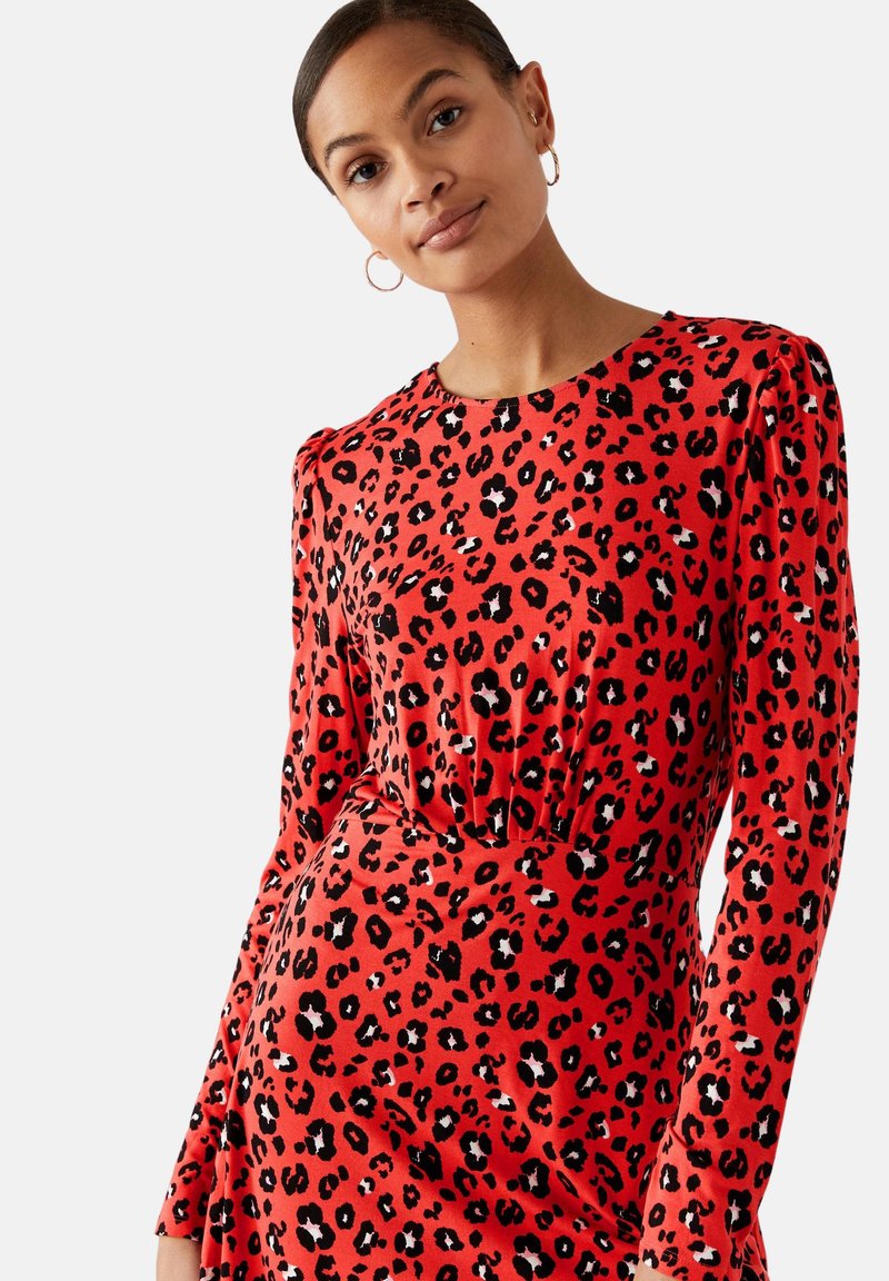 Rotes Kleid mit langen Ärmeln, das ein schwarz-weißes Leopardenmuster aufweist. Glatte Textur und taillierte Passform, mit gerafftem Detail an der Taille.