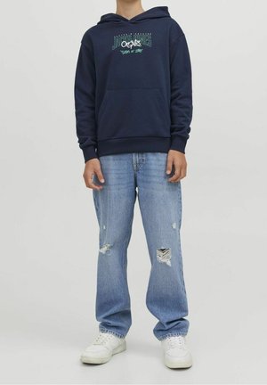 Marineblå hættetrøje med en forlompe og hvid tekst, kombineret med lyseblå slidte jeans og hvide sneakers. Glat stof, afslappet pasform.