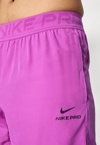 Nike Pro shorts in bright pink fabric with a smooth texture, featuring a black logo on the side and a patterned elastic waistband.