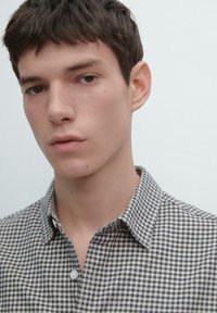 Camicia a quadretti blu navy e bianca con bottoni, dotata di colletto standard, tessuto morbido e vestibilità aderente attorno al collo e alle spalle.