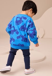 Blue sweatshirt with large dark blue excavator patterns, ribbed cuffs, and hem; paired with dark blue leggings and white sneakers.