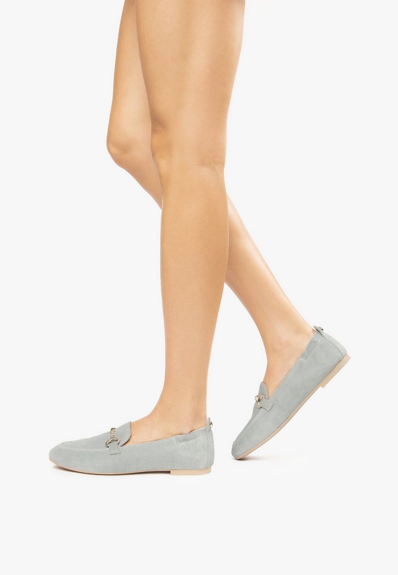 Mocassini in suede grigio chiaro con punta arrotondata, suola piatta e dettagli in hardware dorato decorativo sulla parte superiore.