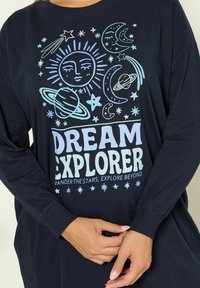 Granatowa koszula z długim rękawem z białym i jasnoniebieskim graficznym wzorem przedstawiającym elementy niebieskie oraz napisem "DREAM EXPLORER". Wykonana z materiału bawełnianego.