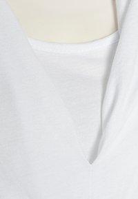 T-shirt branca em V com uma textura suave e leve, com um leve estiramento. O tecido é liso e não possui padrões ou adornos.