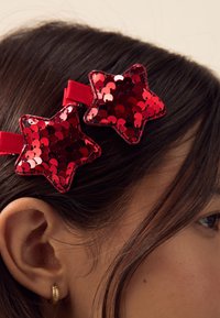 Red sequin star hair clips with a smooth texture, attached to a soft ribbon band, positioned in dark brown hair.