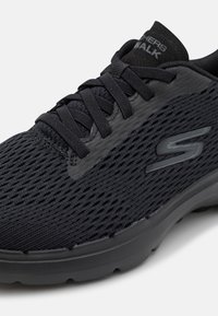 Baskets en maille noire avec dessus texturé, lacets plats et col rembourré. Présentent un design élégant et une semelle coussinée pour le confort.