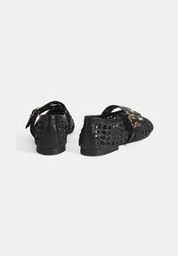 Schwarze Lederschuhe mit einem geflochtenen Oberdesign, flacher Sohle und doppelten Schnallenakzenten. Besondere Merkmale sind die glatte Textur an der Ferse und dem Riemen.