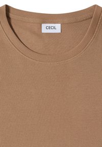 Chemise en tissu côtelé marron avec encolure ronde et étiquette blanche portant la mention "CECIL", cousue à l'intérieur du col.