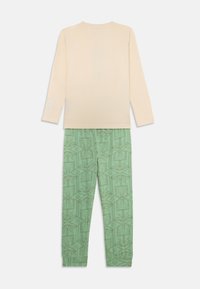 Chemise beige clair à manches longues avec un accent imprimé sur la manche, associée à un pantalon de pyjama vert arborant un motif géométrique répétitif.