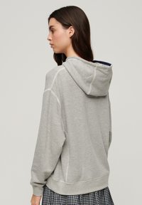 Felpa grigia con cappuccio dal taglio rilassato. Presenta un cappuccio foderato in blu navy, polsini e orlo a costine. Tessuto testurizzato con dettagli di cucitura visibili.