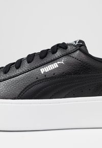 Sneaker nera in pelle con parte superiore testurizzata, suola in gomma bianca, lacci neri prominenti e logo "PUMA" in bianco sul lato.