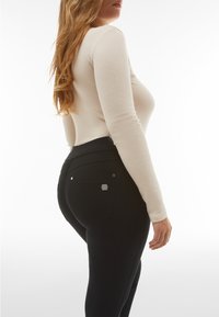 Pantaloni neri a vita alta con una texture liscia e dettagli sui taschini. Top aderente a maniche lunghe in beige chiaro.