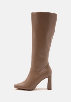 Botte en cuir marron mi-mollet avec bout pointu et talon haut épais, vue de profil sur fond blanc.