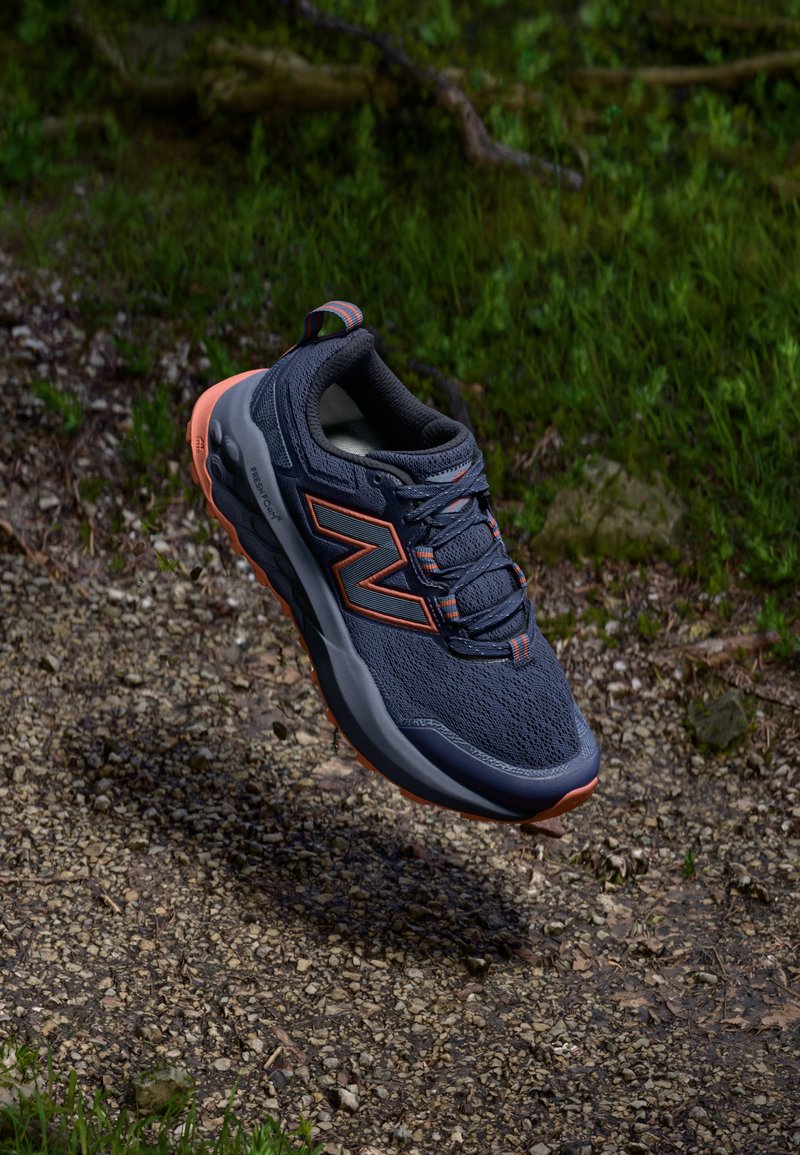 Heren hardloopschoen van ademend navy mesh materiaal met oranje accenten. Beschikt over een ronde neus, een geveerd zool en gestructureerde veters.