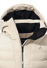 Giacca a collo alto beige imbottita, con fodera nera, chiusura con zip e dettagli perforati all'interno del cappuccio. Presenta un dettaglio del logo sulla parte anteriore.