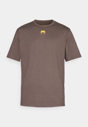Brown cotton t-shirt with a round neckline, short sleeves, and a small yellow graphic of a fang detail on the chest.