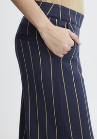 Marineblaue Hosen mit vertikalen goldenen Streifen; aus glattem Stoff gefertigt, mit einer Seitentasche und einem taillierten Bunddesign.