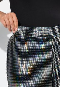 Pantaloni jogger neri con vita elastica, ricoperti di piccole paillettes riflettenti che creano un effetto scintillante e una texture liscia.