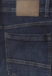 Tmavě modré džíny z denimu s koženou nášivkou se jménem značky, zadní kapsou a zlatými švy.