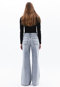 Jeans de mezclilla de tiro alto y acampanados, de color gris claro y con un lavado deslavado, con dos bolsillos traseros y una cintura con lazos para cinturón.