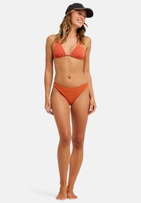 Διμερές μπικίνι σε χρώμα σκουριάς με υφασμένο ζιγκ-ζαγκ σχέδιο. Το πάνω μέρος έχει τριγωνικά cups και λεπτούς ιμάντες· το κάτω μέρος έχει μέτρια κάλυψη.