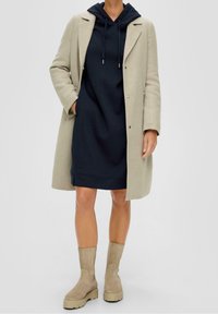 Beige ullkappa över en marinblå hoodieklänning, matchad med ljusbeige mockakängor. Kappan har en skräddarsydd design och knappar.