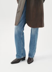 Cappotto con texture a coccodrillo marrone, jeans dritti blu chiaro e stivali marroni con punta a punta e tacco quadrato.