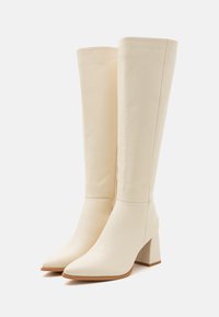 Bottes blanches en cuir jusqu'aux genoux, avec un bout pointu et un talon carré. Texture lisse, coutures minimales et design épuré.