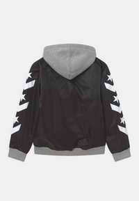 Giacca nera con cappuccio grigio. Presenta motivi bianchi a stelle e strisce sulle maniche. Tessuto liscio con polsini e orlo a costine.