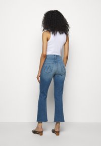 Jeans de color azul claro con cintura alta y parte inferior acampanada, con dos bolsillos traseros que presentan un patrón de costura distintivo. Combinados con una camiseta sin mangas blanca.