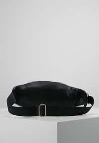 Černá kožená taška s texturovaným povrchem, s fialovou podšívkou a černým nastavitelným popruhem upevněným stříbrnou sponou.