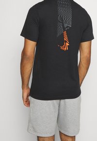 Černé bavlněné tričko s vzorovaným zadním dílem a oranžovými akcenty. Tričko je doplněno šedými šortkami pro ležérní vzhled.