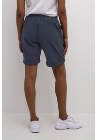 Shorts blu scuro con orlo arrotolato, vita elastica, tasche laterali e tessuto leggero, abbinati a scarpe sportive bianche.